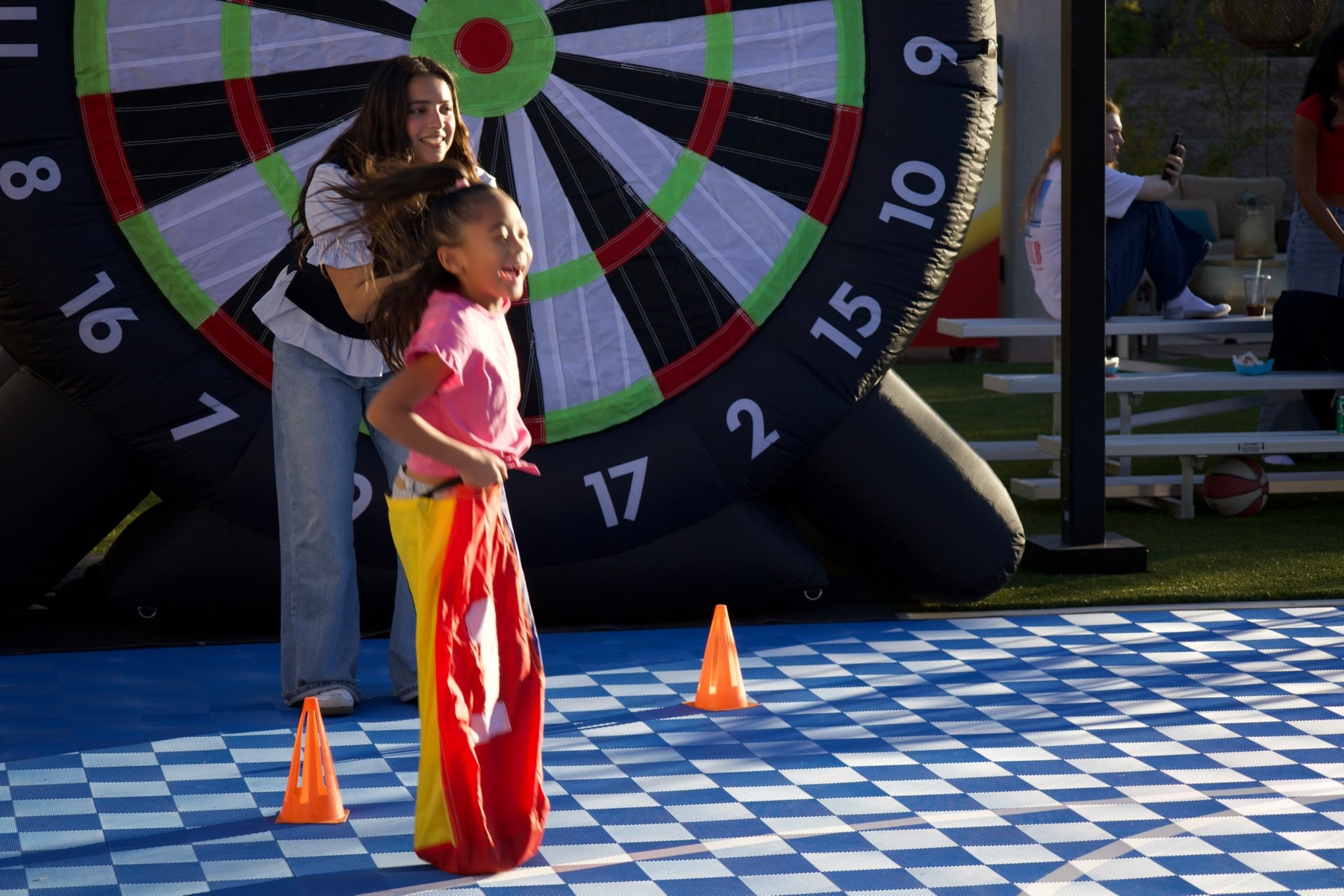 Girl mid-jump in a colorful sack race with giant kick dart behind her