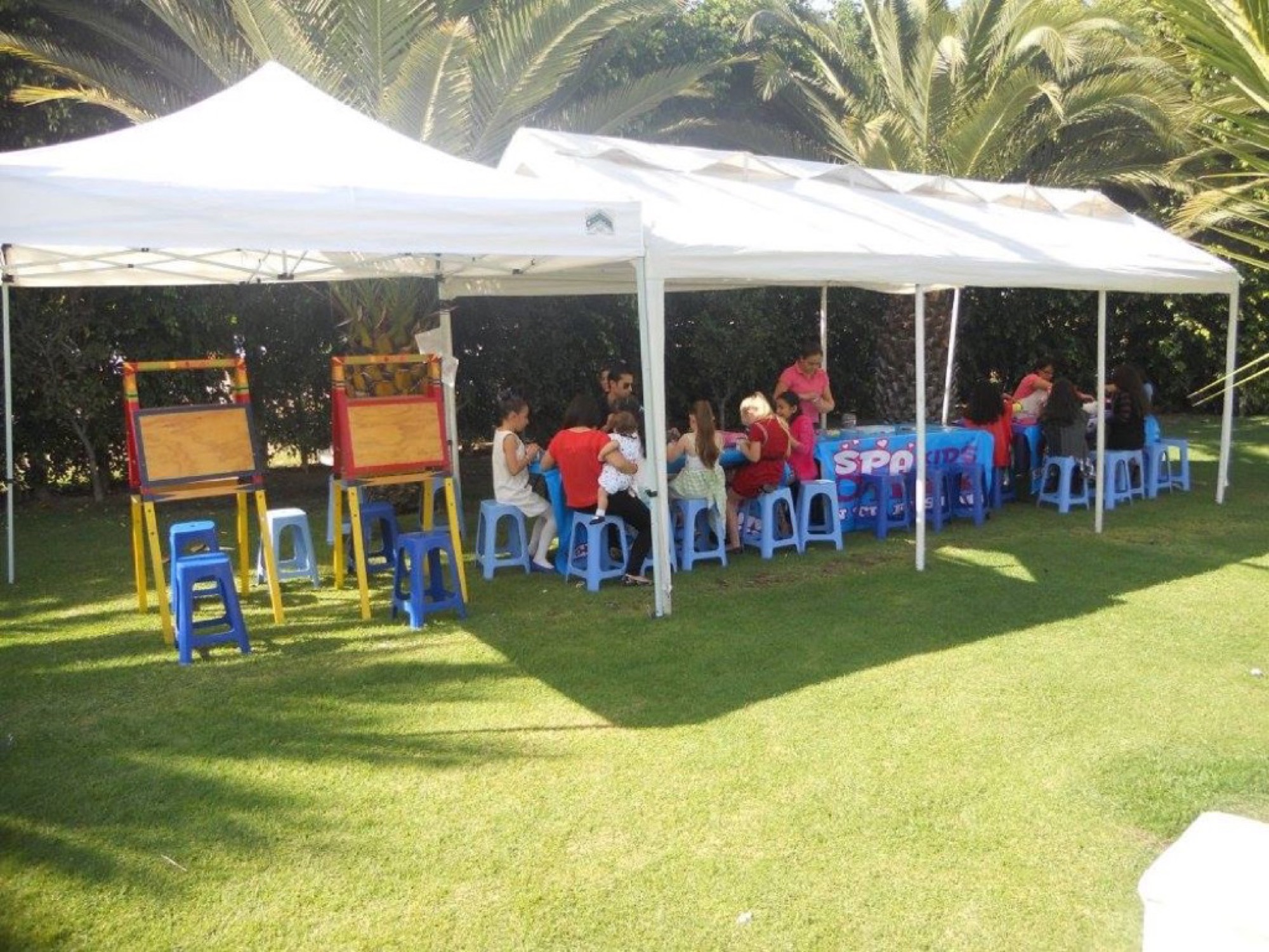 Early kids craft station under white canopy tents with blue stools on a lawn
